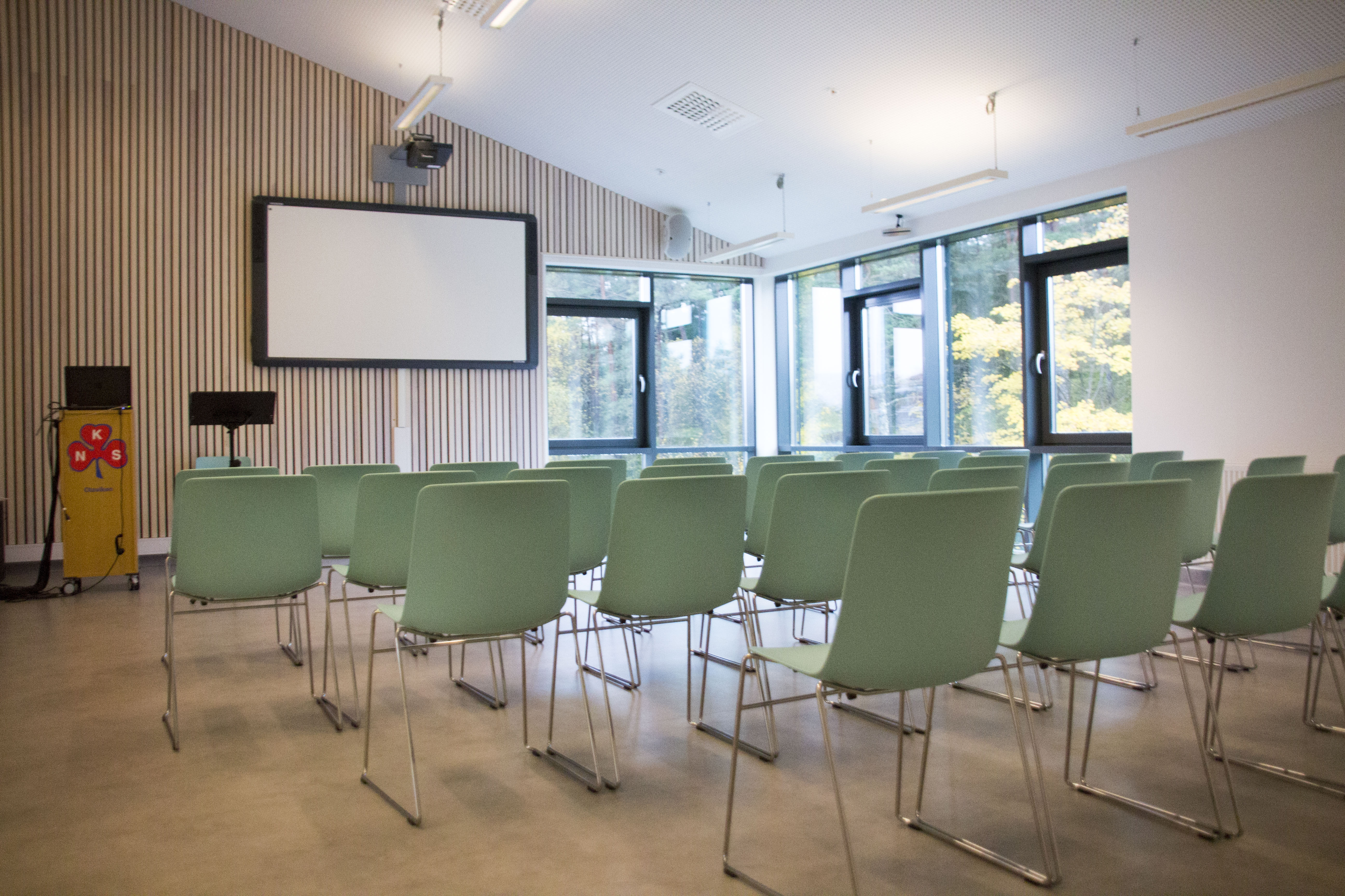 Et rom med grønne stoler og en projektorskjerm