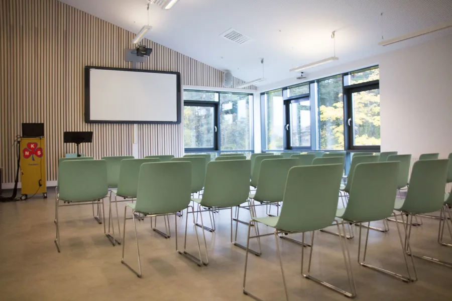 Et rom med grønne stoler og en projektorskjerm