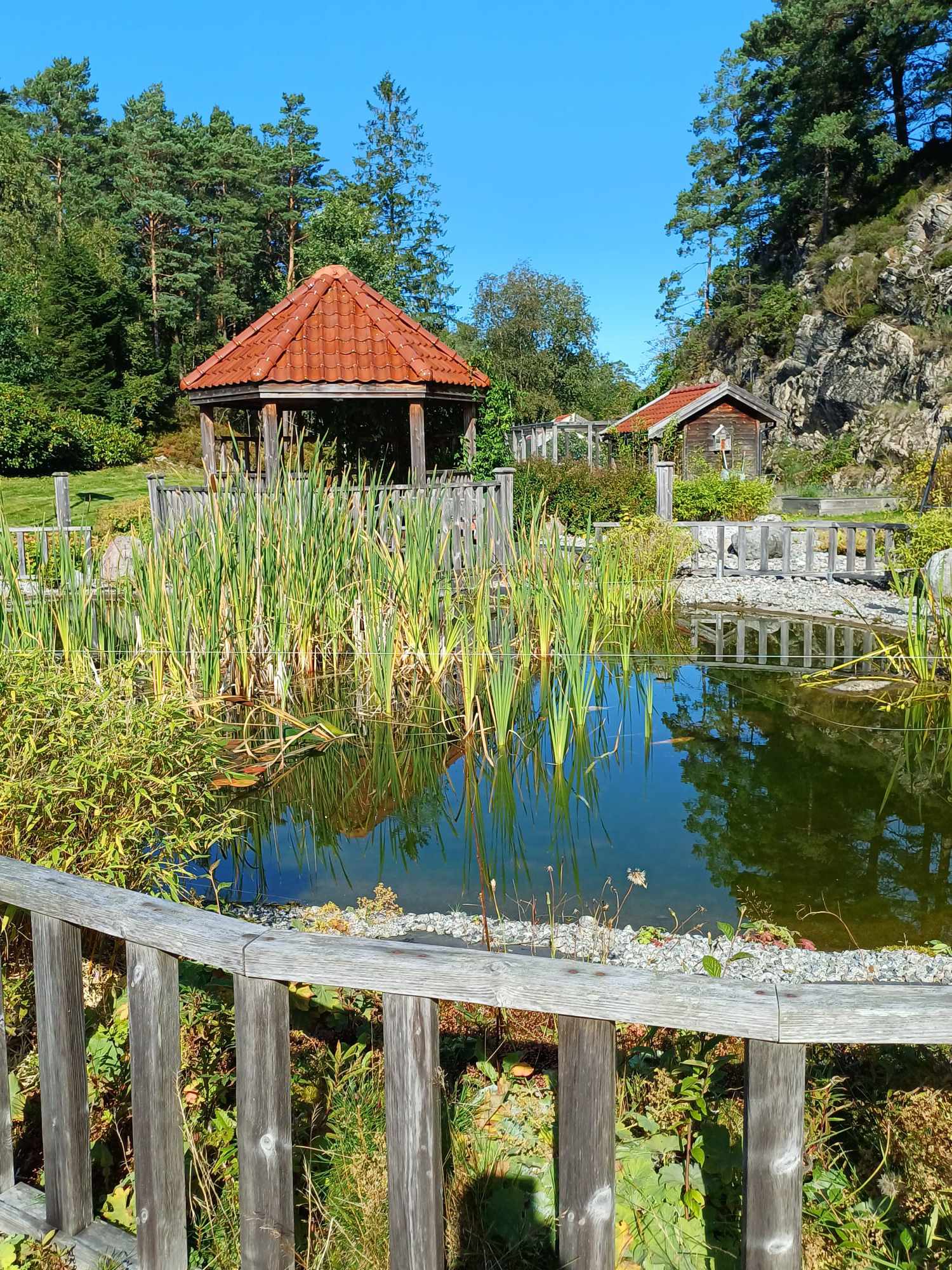 Et tre gjerde foran en dam med et hus i bakgrunnen