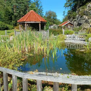 Et tre gjerde foran en dam med et hus i bakgrunnen