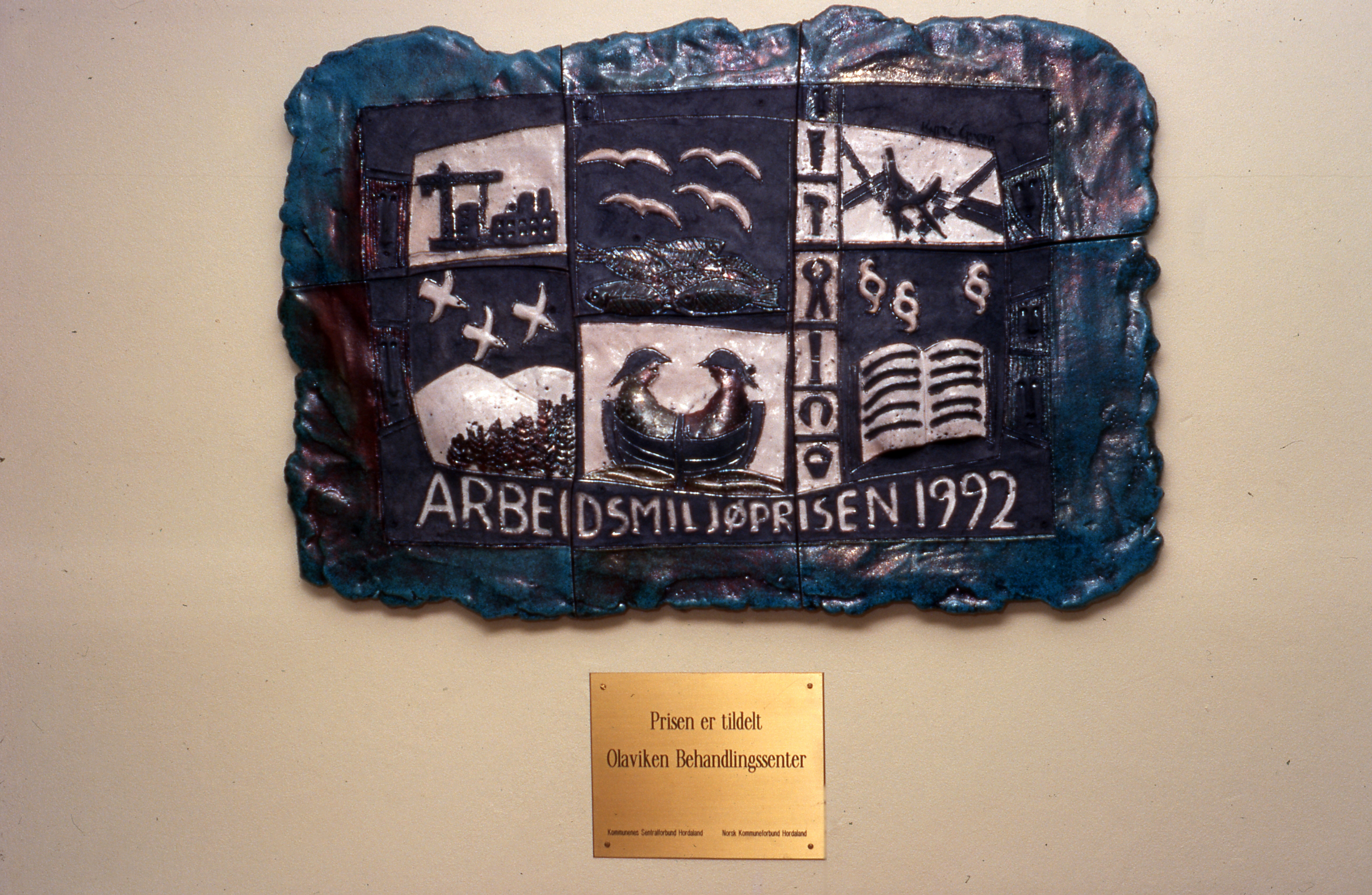 Et bilde i stein med måker, båter og folk