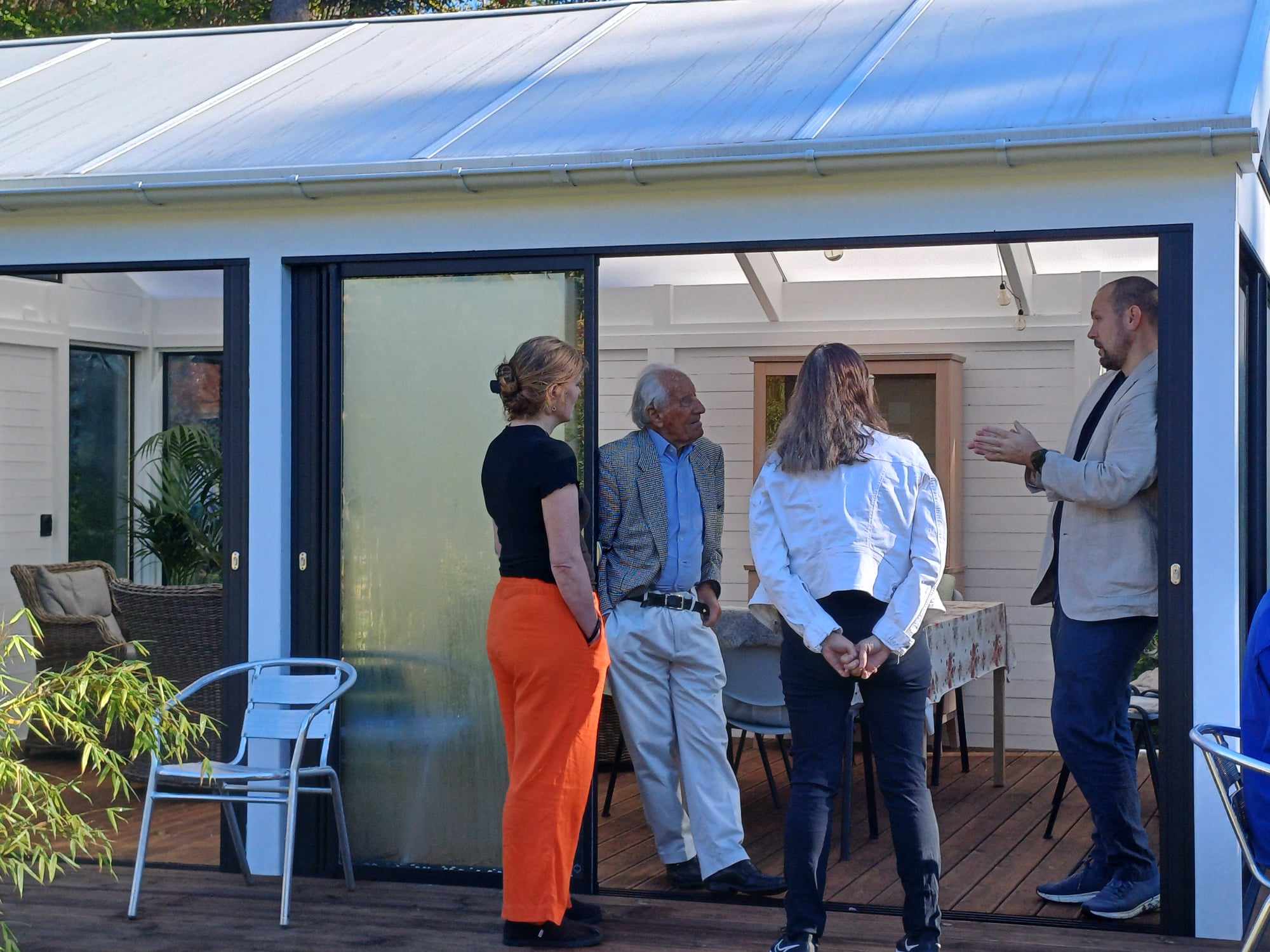 En gruppe mennesker som står utenfor den nye utestuen med glassvegger